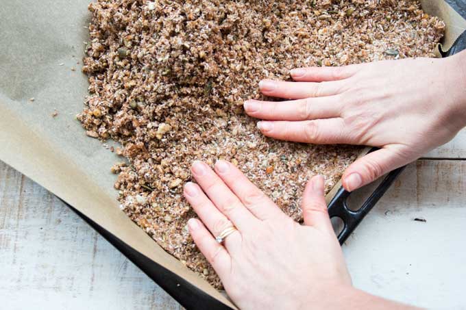 hands pressing down a seed and nut mix onto a baking tray lined with parchment paper