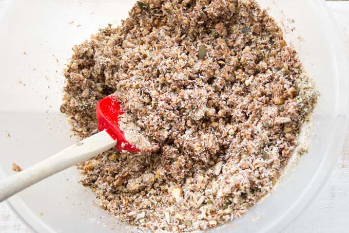 mixing seeds, nuts, peanut butter and coconut in a bowl with a spatula