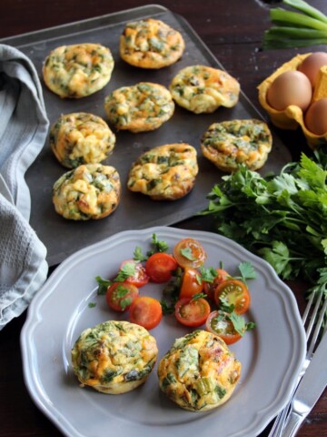 Chorizo Egg Muffins on a baking tray and two muffins with tomato salad on a plate