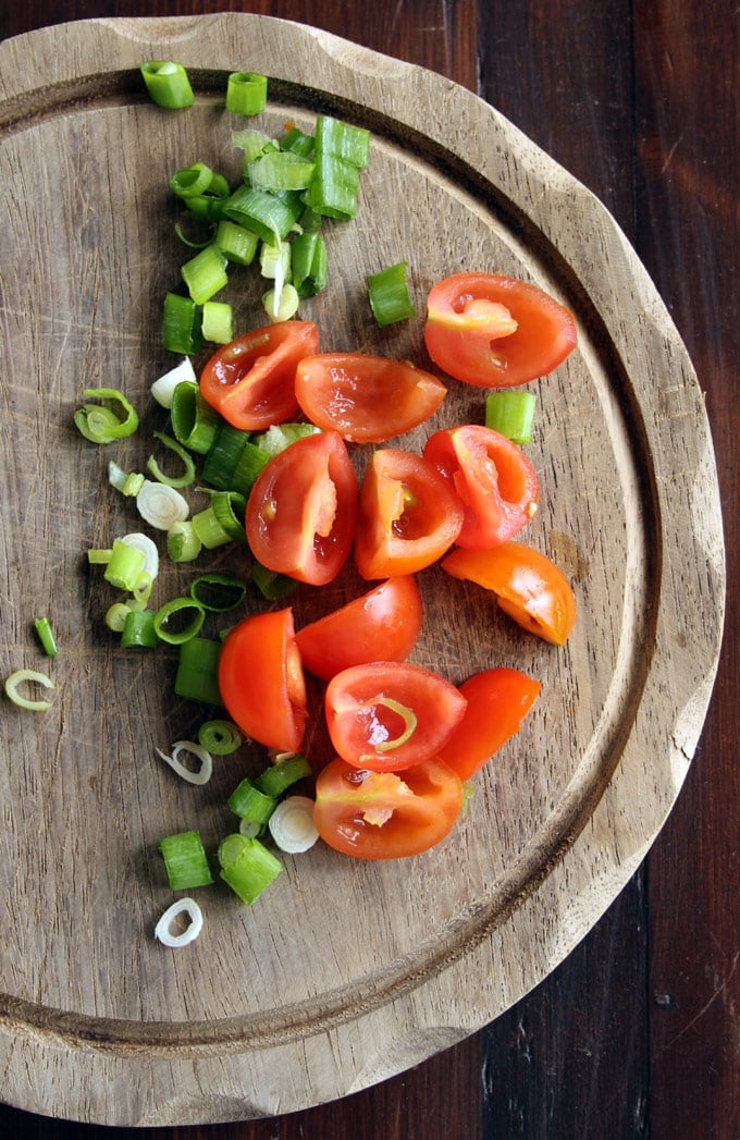 a wooden board with chopped tomatoes and spring onions