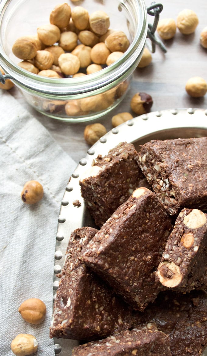 Keto nutella bars cut into squares, arranged in a silver bowl with a jar of shelled hazelnuts in the background