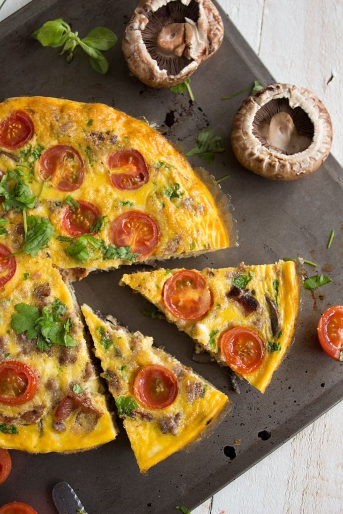 An English breakfast frittata with two slices cut and mushrooms on the side