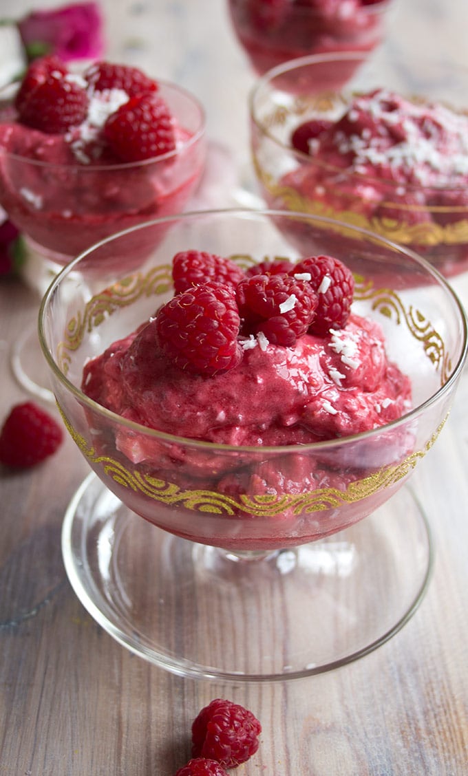 closeup of a glass serving bowl with raspberry frozen yogurt topped with fresh raspberries
