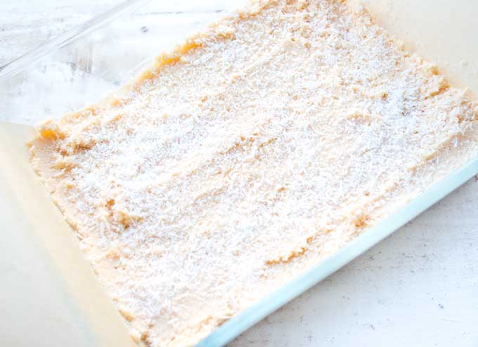 baking dish lined with parchment paper and filled with keto blondie dough topped with desiccated coconut