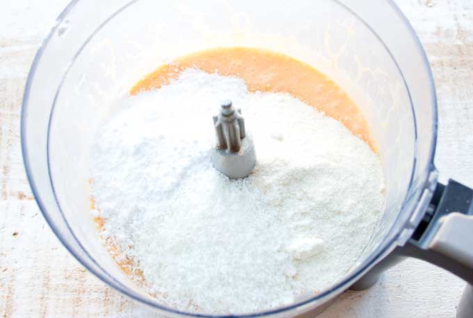 a food processor bowl with mixed wet ingriedients and dry ingredients (coconut flour, desiccated coconut and sweetener)