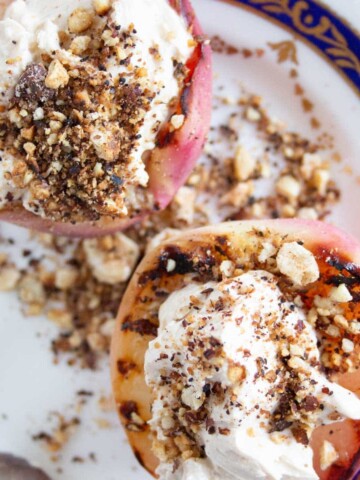 two grilled peach halves topped with mascarpone and hazelnuts