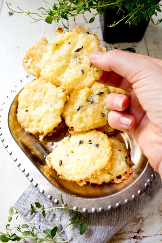 hand holding a cheese thyme keto cracker with a bowl of crackers in the background