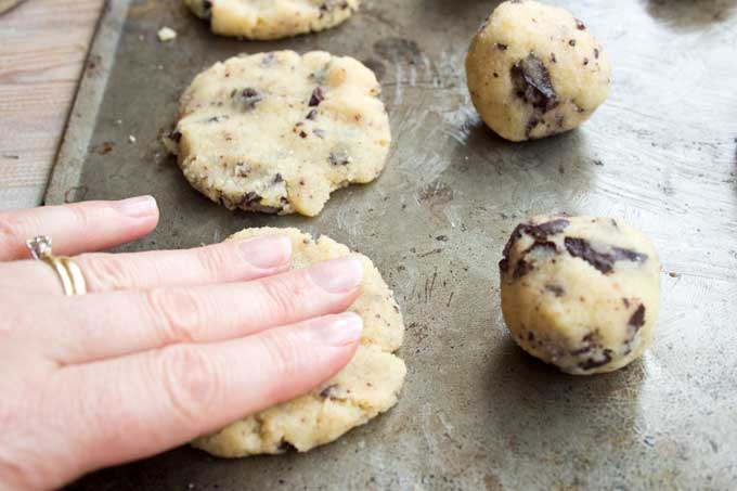A hand flattening balls of cookie dough into a cookie-shape