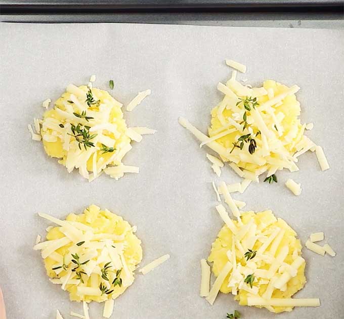 coconut flour crackers on a baking tray lined with parchment paper topped with grated cheese and fresh thyme