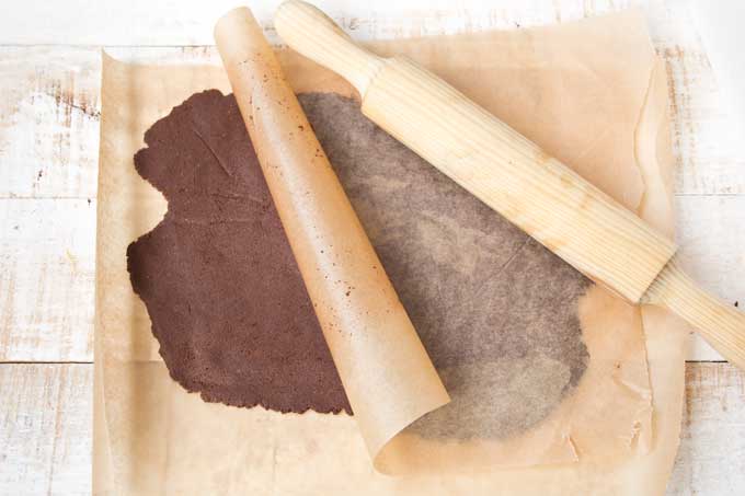 Rolled out cookie dough between 2 sheets of parchment paper with a rolling pin.