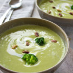 two bowls of broccoli soup with pistachios and broccoli florets