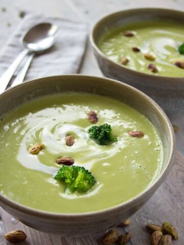 two bowls of broccoli soup with pistachios and broccoli florets