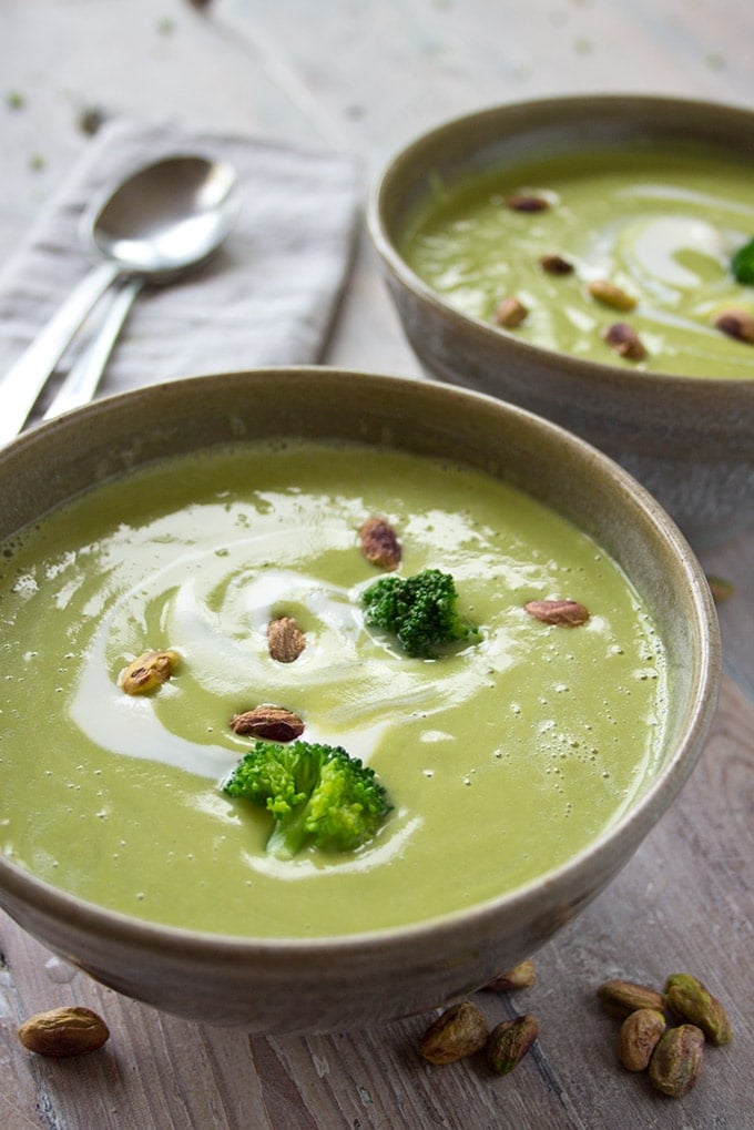 two bowls of broccoli soup with pistachios and broccoli florets