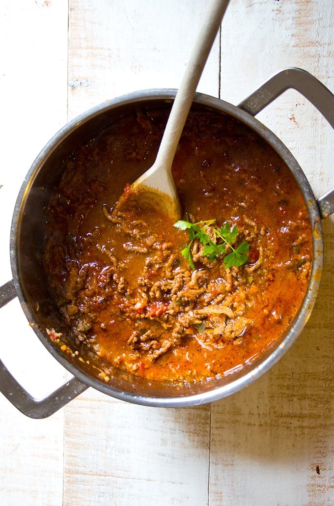 a pot filled with low carb bolognese sauce and a wooden spoon decorated with fresh parsley