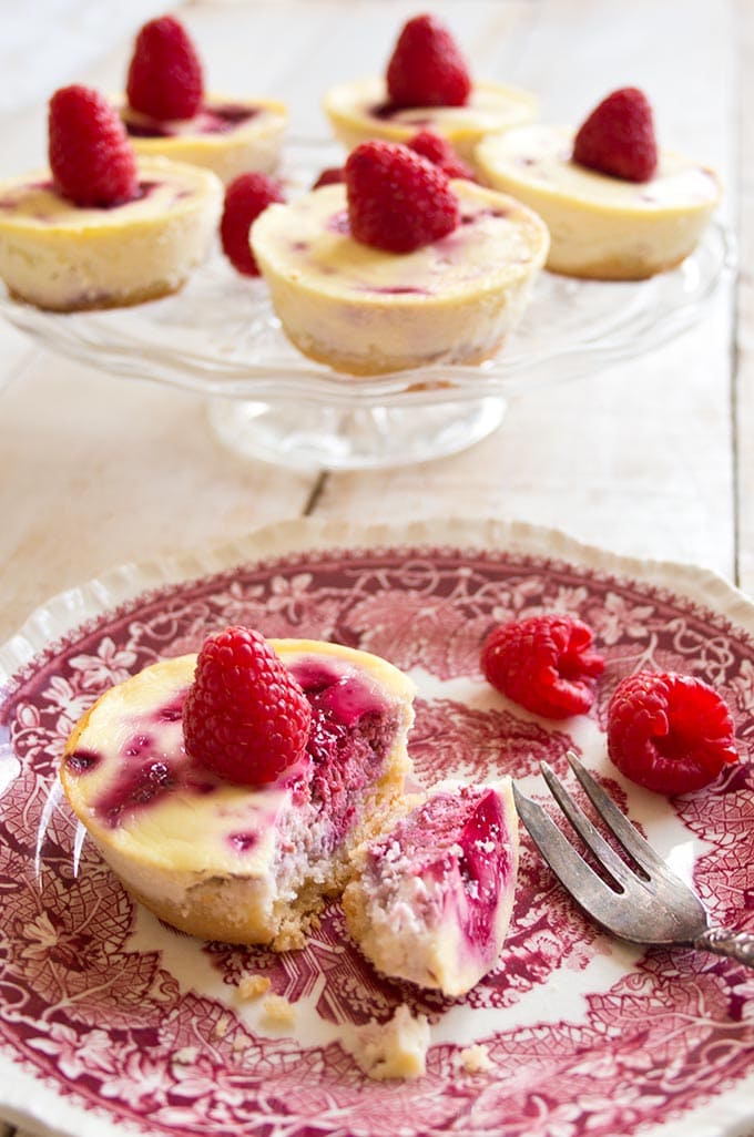 raspberry cheesecakes on a cake stand and one cake on a plate