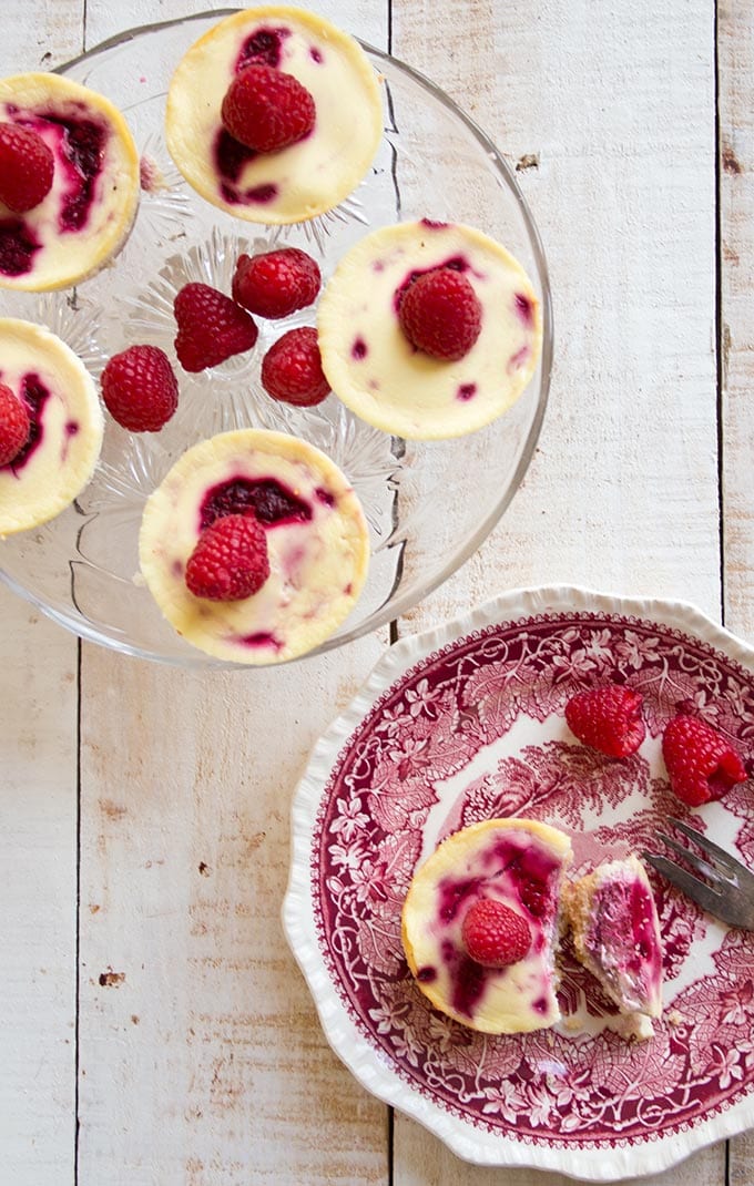 a cake stand with individual low carb raspberry cheesecakes and a raspberry cheesecake on a plate