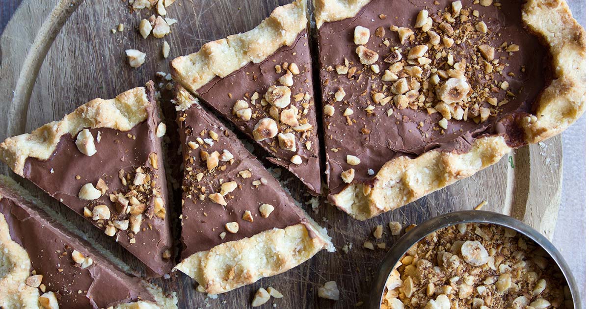 a chocolate tart cut into slices and topped with hazelnuts