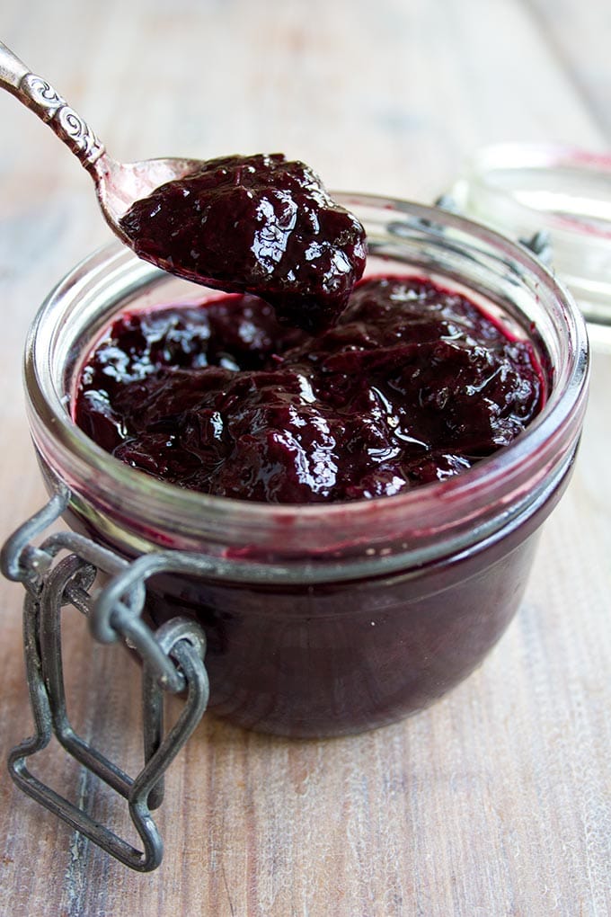 A spoon of sugar free blueberry jam over a full blueberry jam jar
