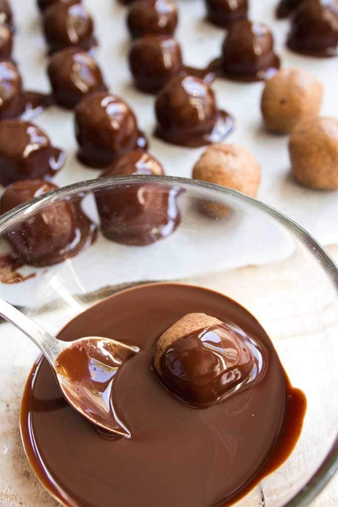 dipping almond butter keto truffles into a bowl with melted low carb chocolate
