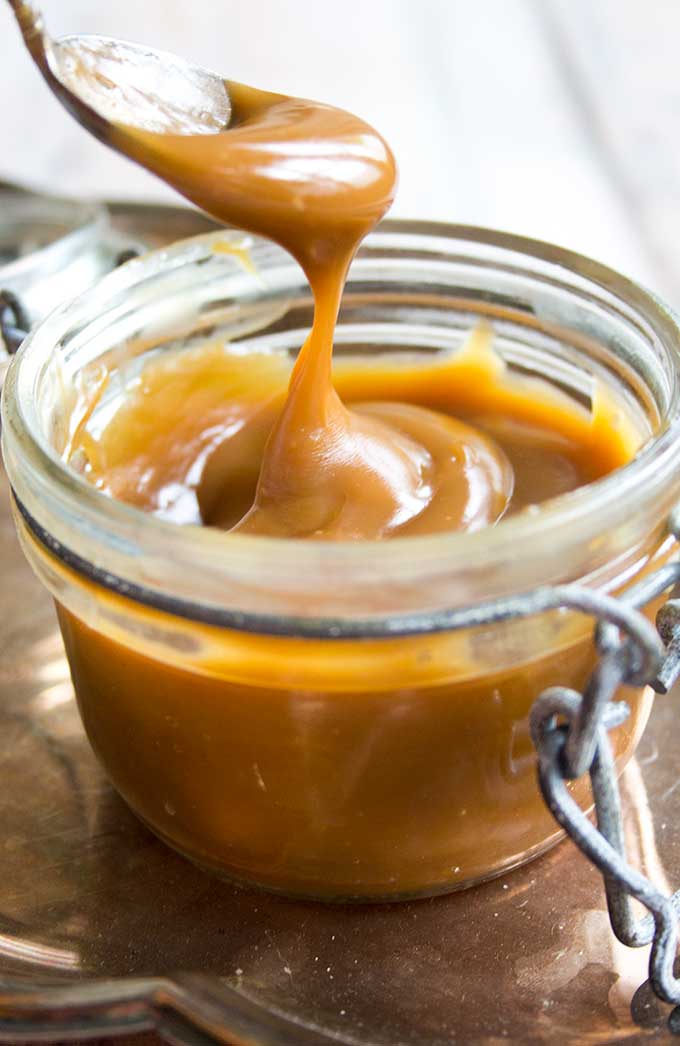 A spoon taking sugar free caramel sauce out of a glass jar 
