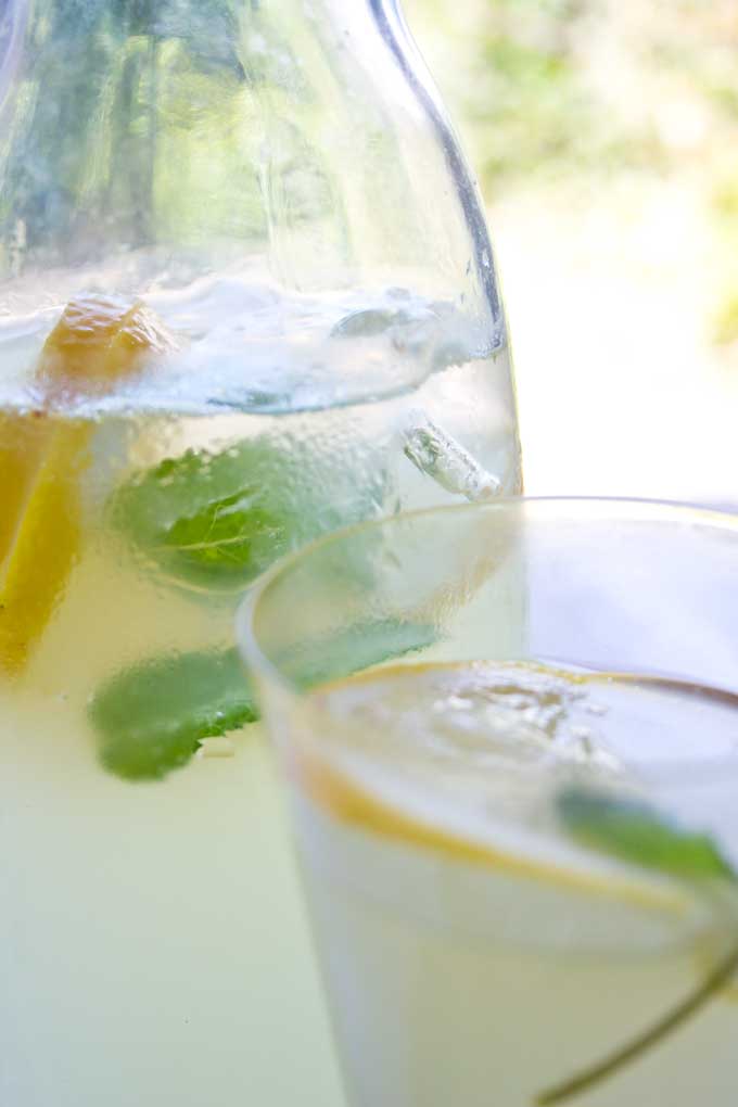 a glass jug of sugar free homemade ginger ale with mint leaves, ice cubes and lemon slices