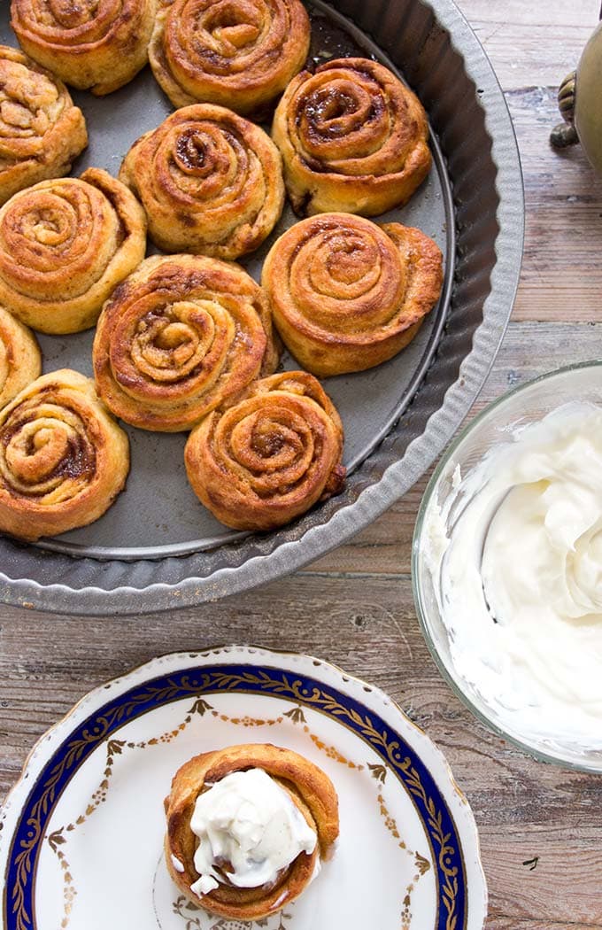 uma bandeja com rolos de canela keto e um rolo de canela com cobertura de cream cheese num prato