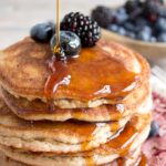 a stack of pancakes decorated with berries and sugar free syrup drizzle