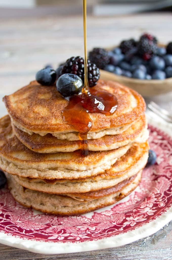 drizzling sugar free syrup over a stack of pancakes on a plate