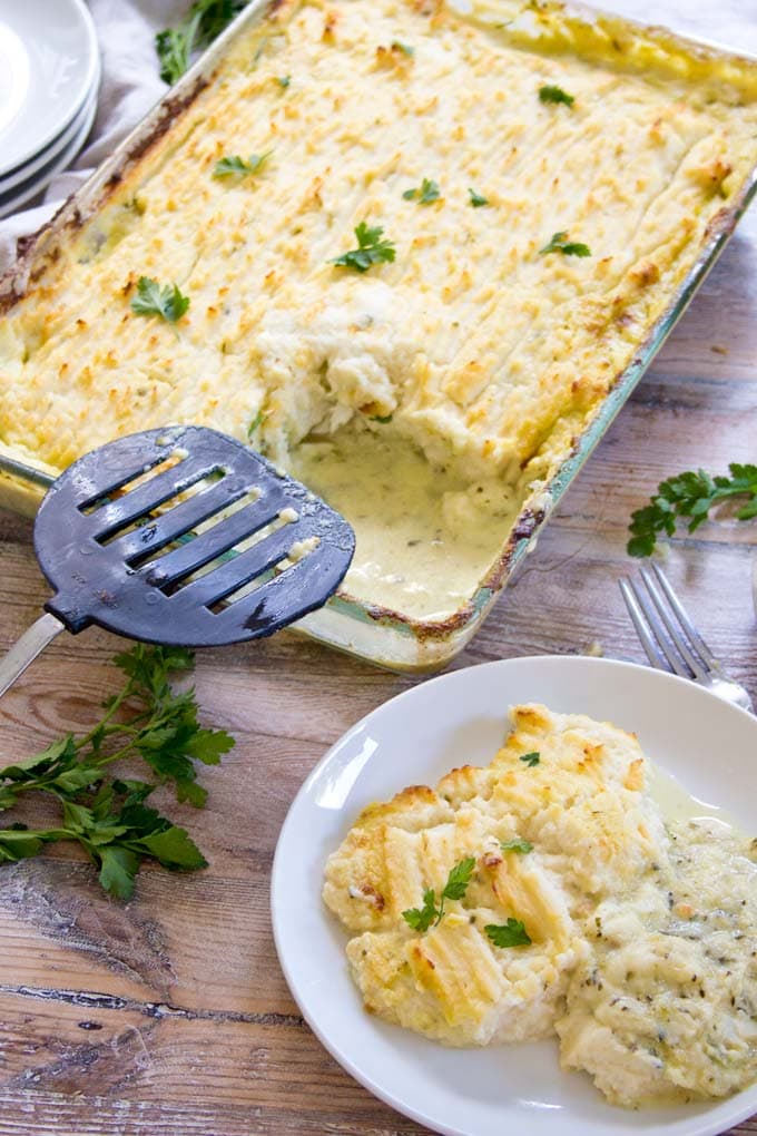 a casserole with low carb fish pie and cauliflower mash crust with a spatula and a plate with a portion of fish pie