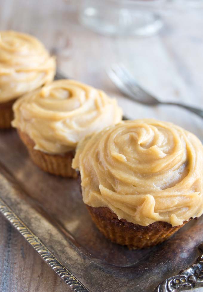 3 gingerbread cupcakes with caramel frosting in a row on a silver tray.