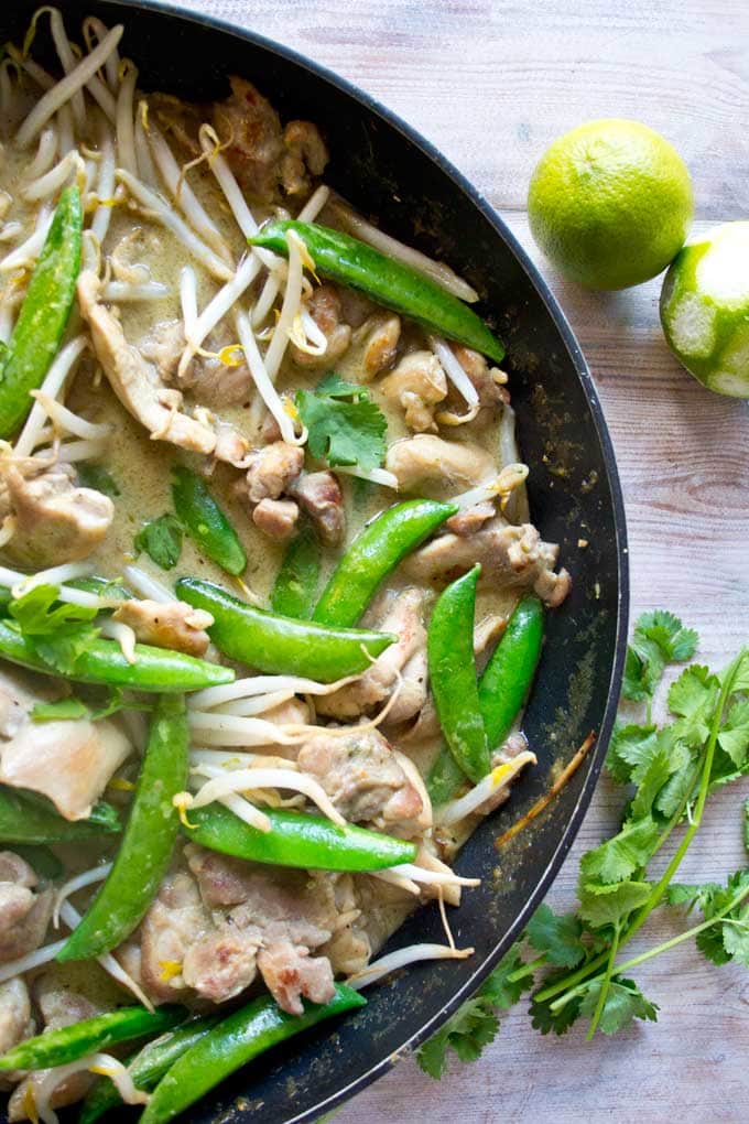closeup of a pan containing green curry with chicken, bean sprouts and sugarsnap peas
