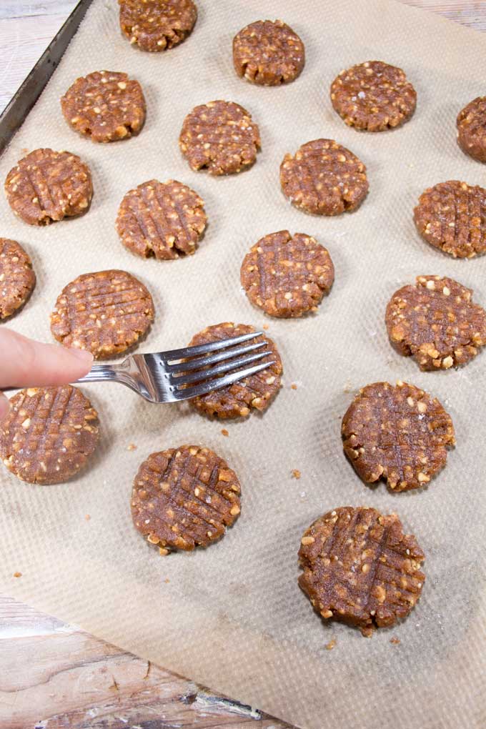 a fork pressing a criss-cross pattern on unbaked low carb Keto peanut butter cookies on a lined baking tray 