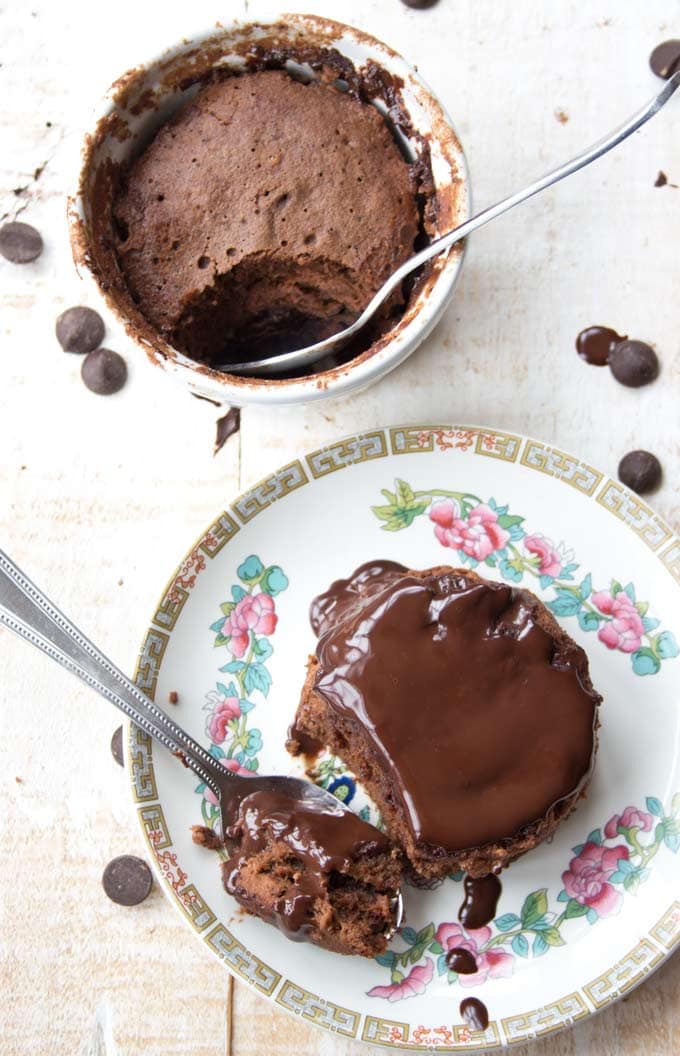Two keto chocolate mug cakes - one on a plate with chocolate sauce and another one in a ramekin