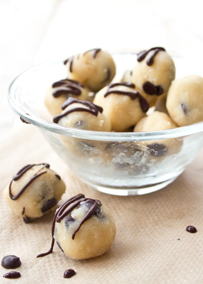 A glass bowl with small balls of edible cookie dough, some decorated with chocolate ganache