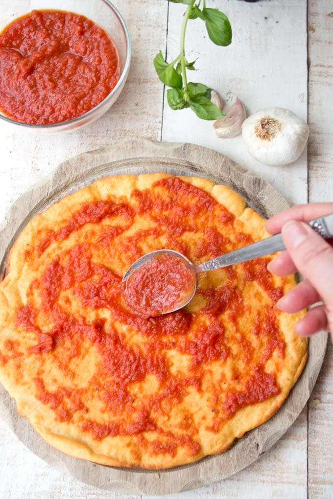 Pizza base being spread with Tomato Sauce with a spoon