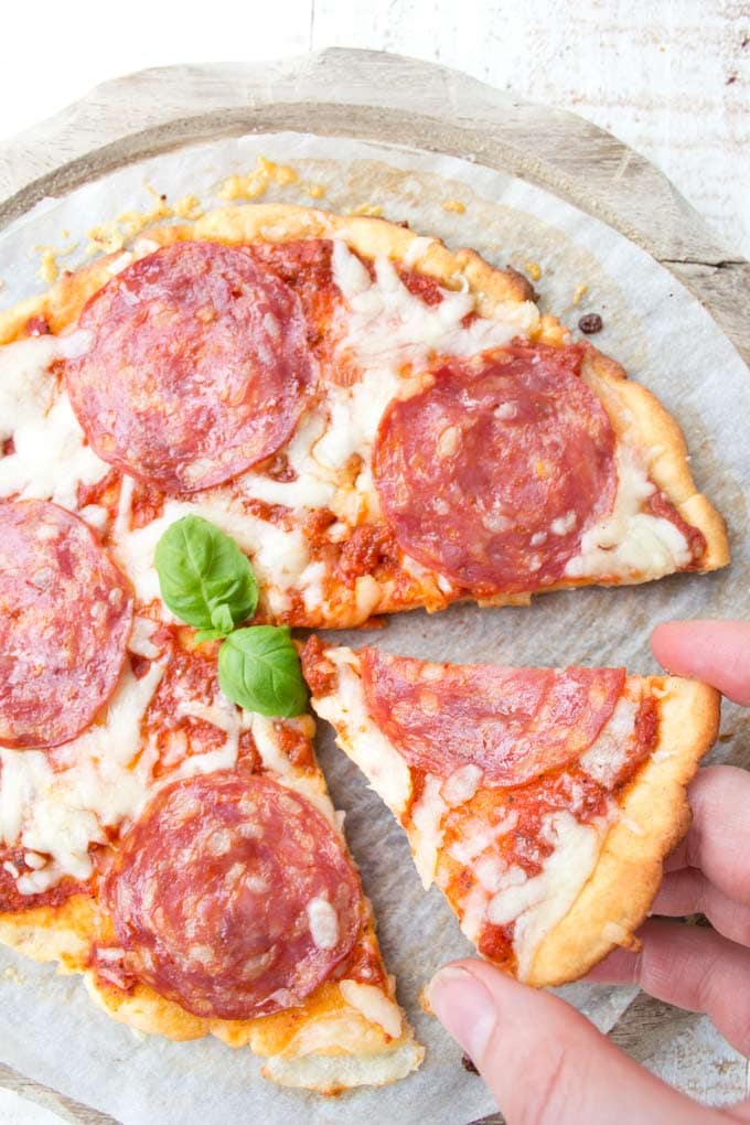 A hand taking a slice from a low carb pizza topped with marinara sauce, mozzarella and salami