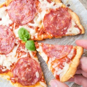 a low carb pizza topped with mozzarella and salami and a hand taking a slice