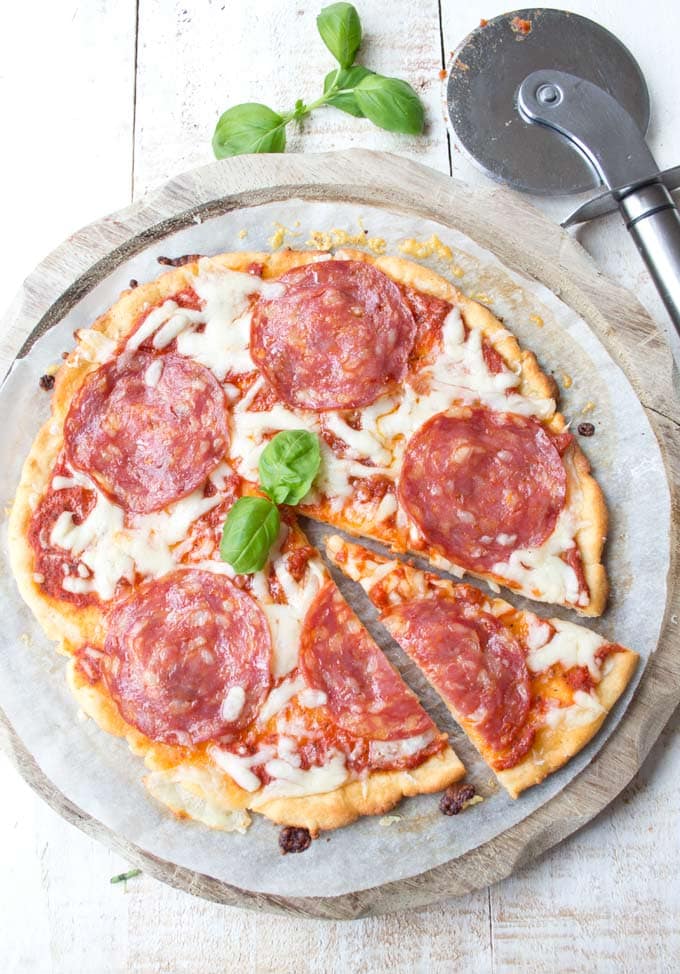 A baked low carb pizza topped with salami with a slice cut out and a pizza cutter on the side