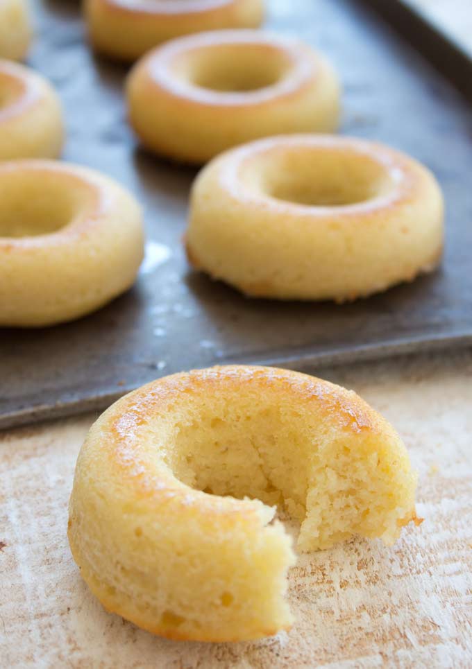 a bitten donut in the foreground showing the moist inside. In the background more keto donuts on a baking tray 