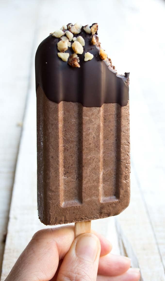 A sugar free chocolate fudgesicle with one bite missing, held up by a hand