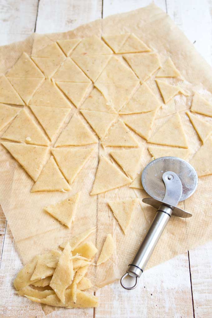 Rolled out dough for cut into triangles with a pizza cutter and offcuts on the side 