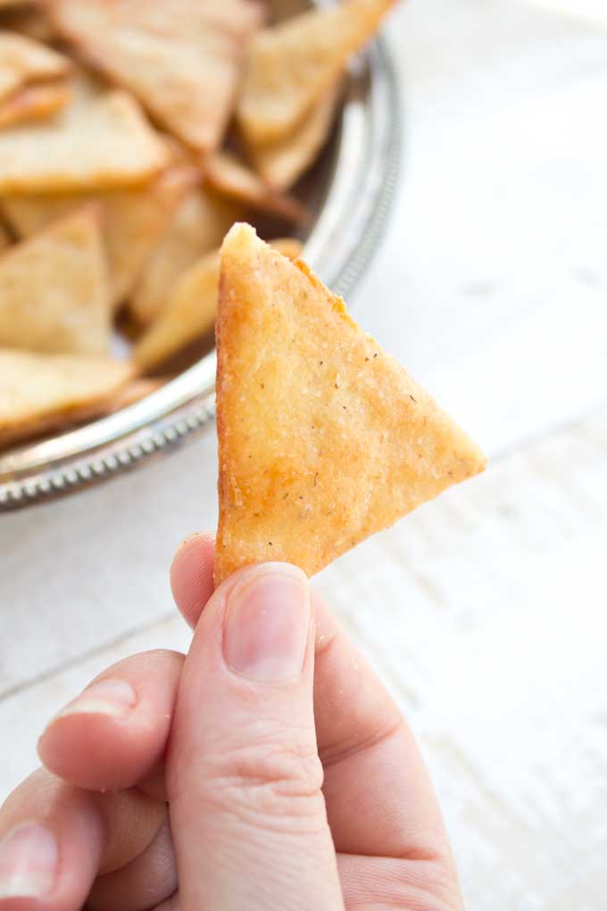 Closeup of a hand holding up a low carb tortilla chip between thumb and index finger