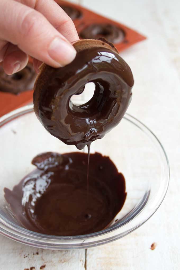 A Keto chocolate donut being dipped in chocolate glaze
