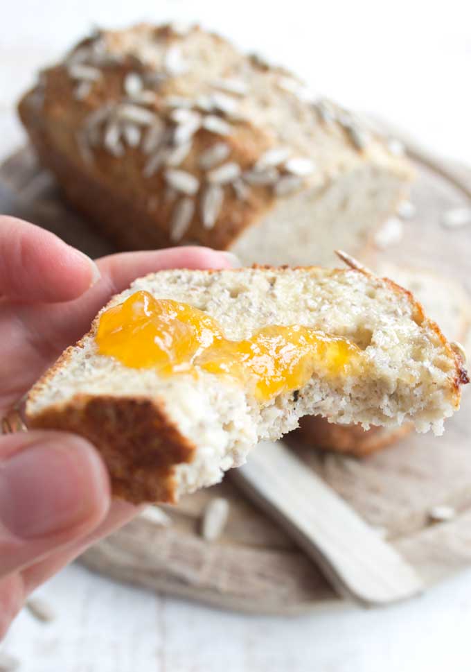 Hand holding a half-eaten slice of chia almond low carb bread topped with butter and jam 