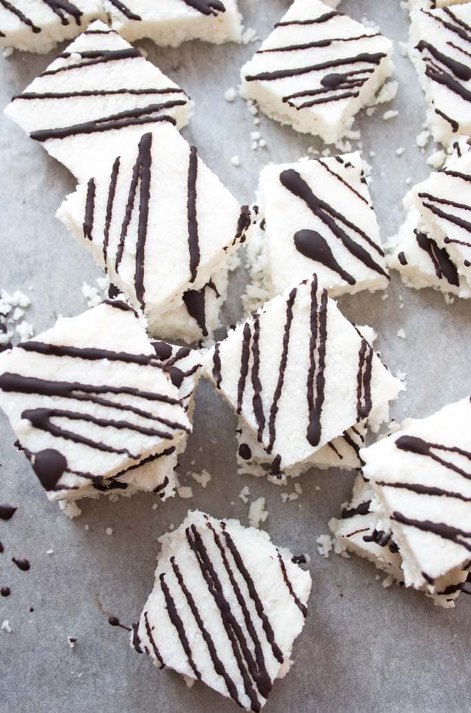 Keto coconut bars with chocolate drizzle stacked on a lined baking pan