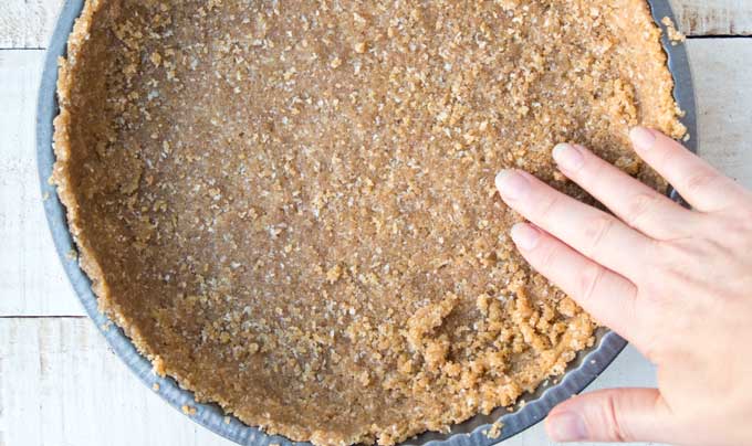 pressing the dough for the pie crust into the pan with hands