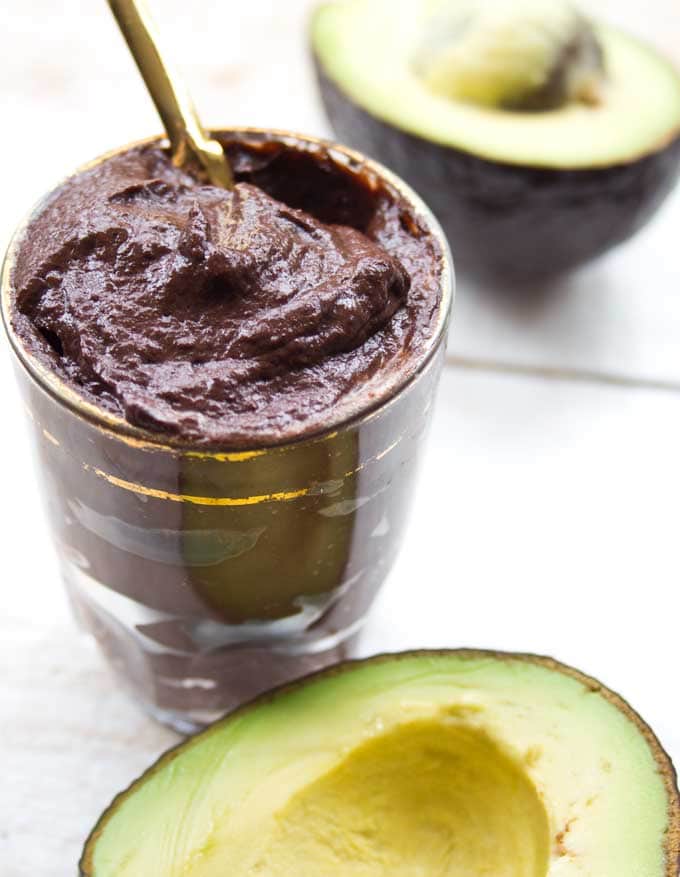 a desert portion of chocolate avocado mousse with a spoon and two halves of avocado