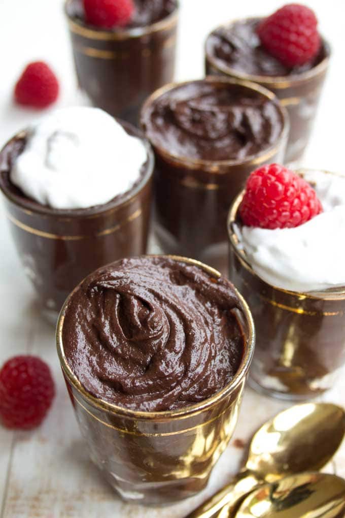 glasses with chocolate avocado mousse decorated with raspberries and spoons on the side