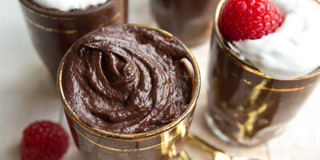 shot glasses with chocolate avocado mousse decorated with coconut cream and raspberries