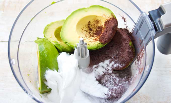 a bowl with ingredients for chocolate avocado mousse - avocado, cocoa powder, powdered sweetener and coconut cream